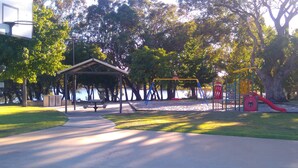 Ein Park mit Spielplatz, Picknicktischen und einem überdachten Sitzbereich.