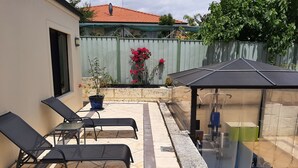 Eine Terrasse mit zwei Liegestühlen, einem kleinen Tisch, einer überdachten Sitzecke und einem Blumentopf.