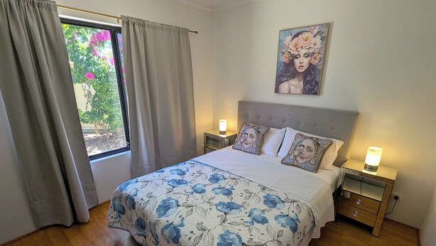 Ein Schlafzimmer mit einem Bett, zwei Nachttischen, einem Fenster mit Vorhängen und einem Bild an der Wand.