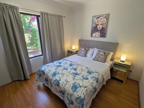 Quarto com cama, duas mesas de cabeceira, um criado-mudo, uma janela com cortinas e um quadro na parede.