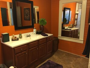 A bathroom with a white sink, wooden cabinets, a large mirror, and a potted plant.
