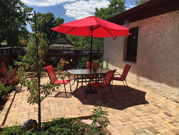 A patio with a table and chairs, a red umbrella, and a brick floor.