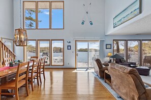 A spacious living area with a wooden dining table, a brown leather sofa, and a view of a body of water through large windows.