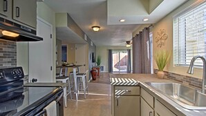 A kitchen with a stove, sink, and bar stools. - East Tucson Home w/ Backyard, Patio & Fire Pit (Tucson)