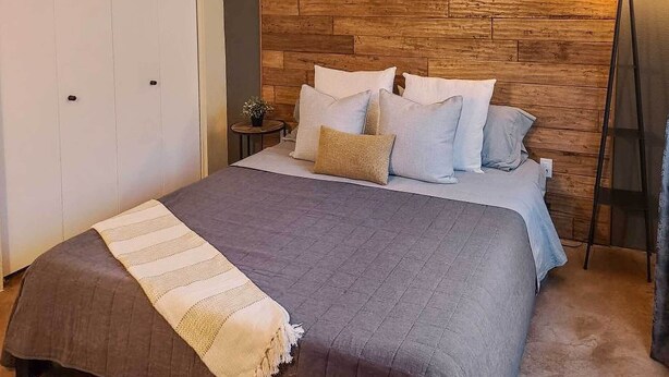 A bedroom with a wooden headboard, a bed with multiple pillows, a bedside lamp, and a small table with a plant. - East Tucson Home w/ Backyard, Patio & Fire Pit (Tucson)