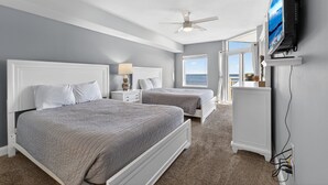 A bedroom with two beds, a ceiling fan, a TV, and a view of the ocean. - Myrtle Beach Vacation | Pool & Ocean Views | Summer Sun | OB 502 (Myrtle Beach)