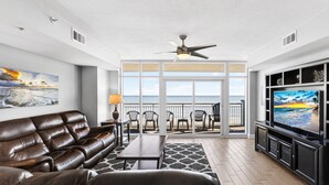 A living room with a leather sofa, a coffee table, and a TV. There are chairs and a table outside the room, with a view of the ocean. - Myrtle Beach Vacation | Pool & Ocean Views | Summer Sun | OB 502 (Myrtle Beach)
