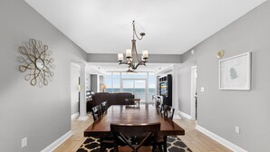 A dining area with a large wooden table, chairs, a chandelier, and a patterned rug. - Myrtle Beach Vacation | Pool & Ocean Views | Summer Sun | OB 502 (Myrtle Beach)