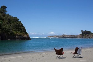 Una playa con dos sillas mirando al océano, un litoral rocoso y cielos despejados.