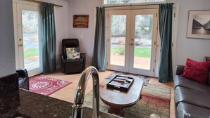 A living room with a view of a river, a black leather chair, a wooden coffee table, and a red throw pillow on a leather sofa. - Beautiful two bedroom one bath house overlooking the Siuslaw river. (Mapleton)