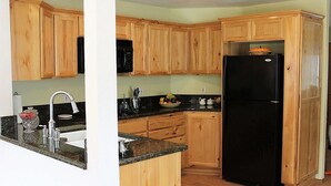 A kitchen with wooden cabinets, a black refrigerator, granite countertops, and a microwave. - Beautiful two bedroom one bath house overlooking the Siuslaw river. (Mapleton)