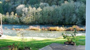 A wooden deck overlooking a river with a forested hillside in the background. - Beautiful two bedroom one bath house overlooking the Siuslaw river. (Mapleton)