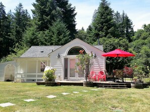 A small, single-story building with a porch, a red umbrella, and outdoor seating. - Beautiful two bedroom one bath house overlooking the Siuslaw river. (Mapleton)