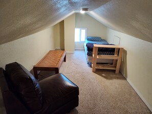 A small attic bedroom with a bed, a wooden table, a bench, and a leather couch. - Beautiful two bedroom one bath house overlooking the Siuslaw river. (Mapleton)