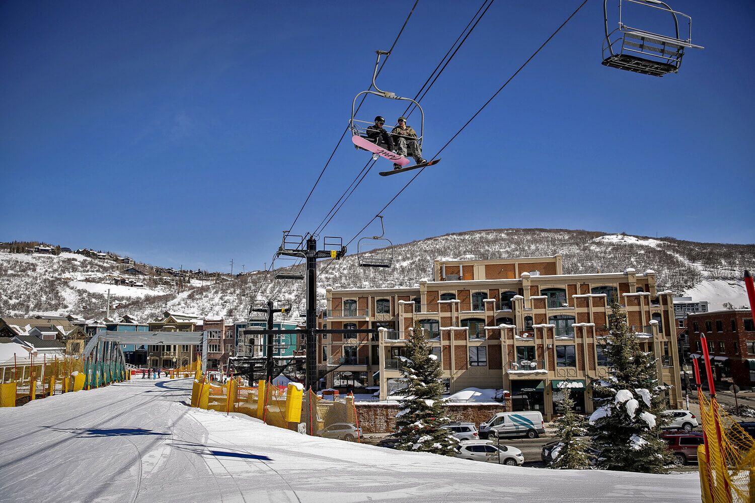 Ski-in convenience meets alpine charm at the base of the mountain, with the chairlift delivering riders directly to the slopes and modern condos nestled against snowy peaks.