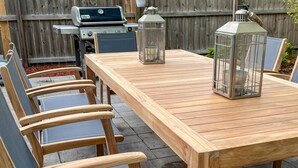 Een houten tuintafel met stoelen, een barbecue en lantaarns.