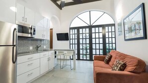 Cocina moderna con armarios blancos, refrigerador de acero inoxidable y televisor de pantalla plana. Amplia ventana arqueada que proporciona luz natural y vistas al exterior.