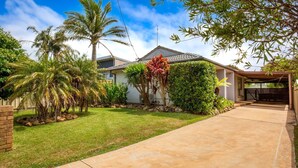 Una casa residenziale con un prato curato, palme e un vialetto coperto.