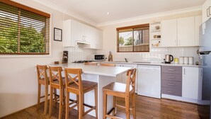 Una cocina moderna con armarios blancos, una isla central con taburetes de bar, microondas y lavavajillas.