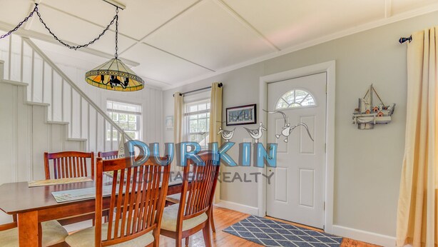 A dining area with wooden chairs and a table, a staircase, and a door with a decorative window.