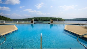Ein klares, blaues Schwimmbecken mit einer Holzterrasse, umgeben von einem weißen Zaun und Bäumen im Hintergrund.