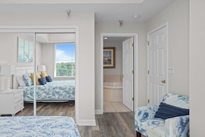 A bedroom with a bed, bedside tables, a chair, a bathroom with a bathtub, and a door leading to another room. - Towers 9106 - Four Bedroom Apartment, Sleeps 10 (Osage Beach)