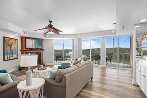 A spacious living room with a large sofa, a fireplace, and a balcony with a view of the forest. - Towers 9106 - Four Bedroom Apartment, Sleeps 10 (Osage Beach)