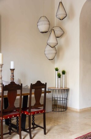 A dining area with a wooden table and chairs, a round side table with decorative vases, and hanging pendant lights.