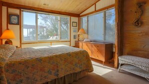 A bedroom with a bed, a desk, a chair, and large windows. - See, Hear & Feel the Ocean from this Beach Bungalow with Private Multi-Level Deck & Swing Chair! (Folly Beach)