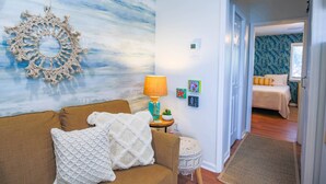 Un salón con un sofá marrón, un plaid blanco de punto, una lámpara azul y una pared con un diseño abstracto azul y blanco.