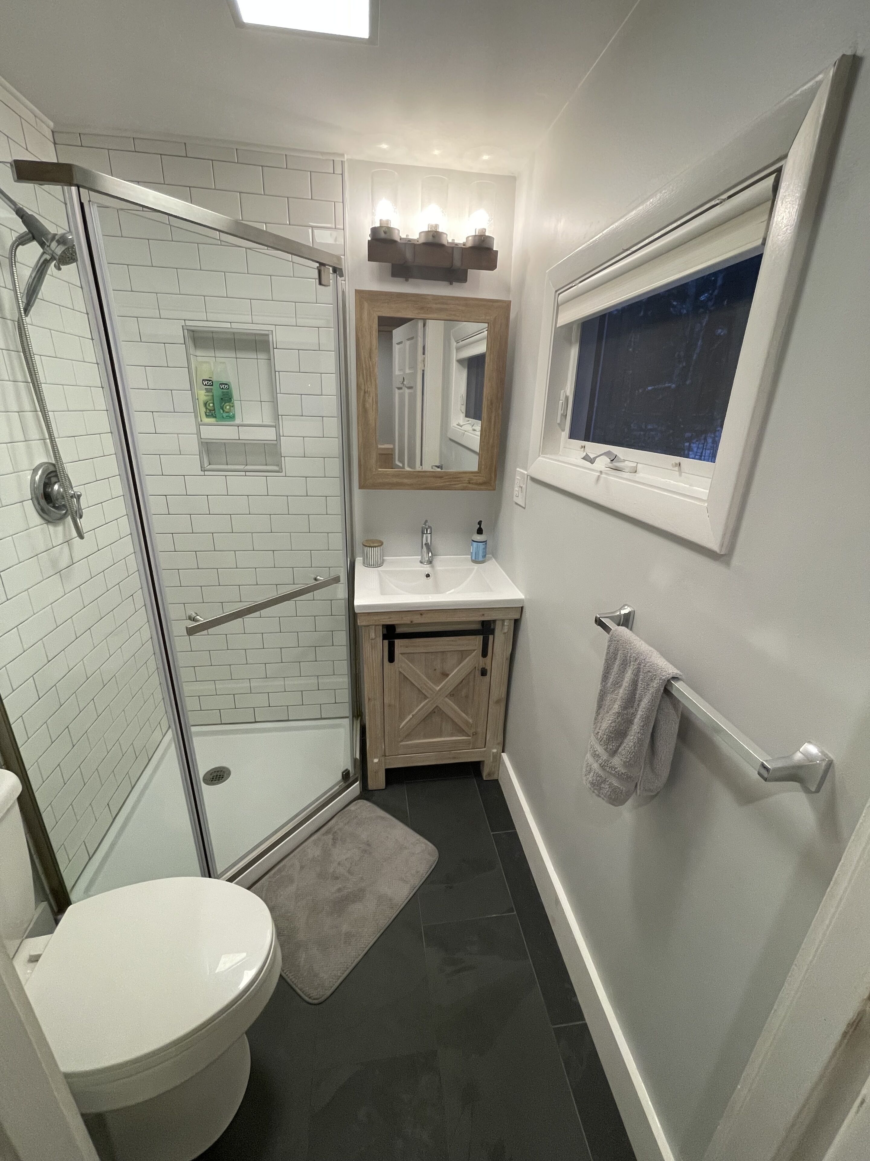 A bathroom with a glass shower enclosure, a white toilet, a sink with a mirror above it, and a towel rack.