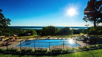 A swimming pool with a view of the sea, surrounded by a fence and greenery.