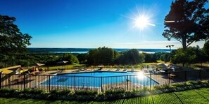 Une piscine avec vue sur la mer, entourée d’une clôture et de verdure.