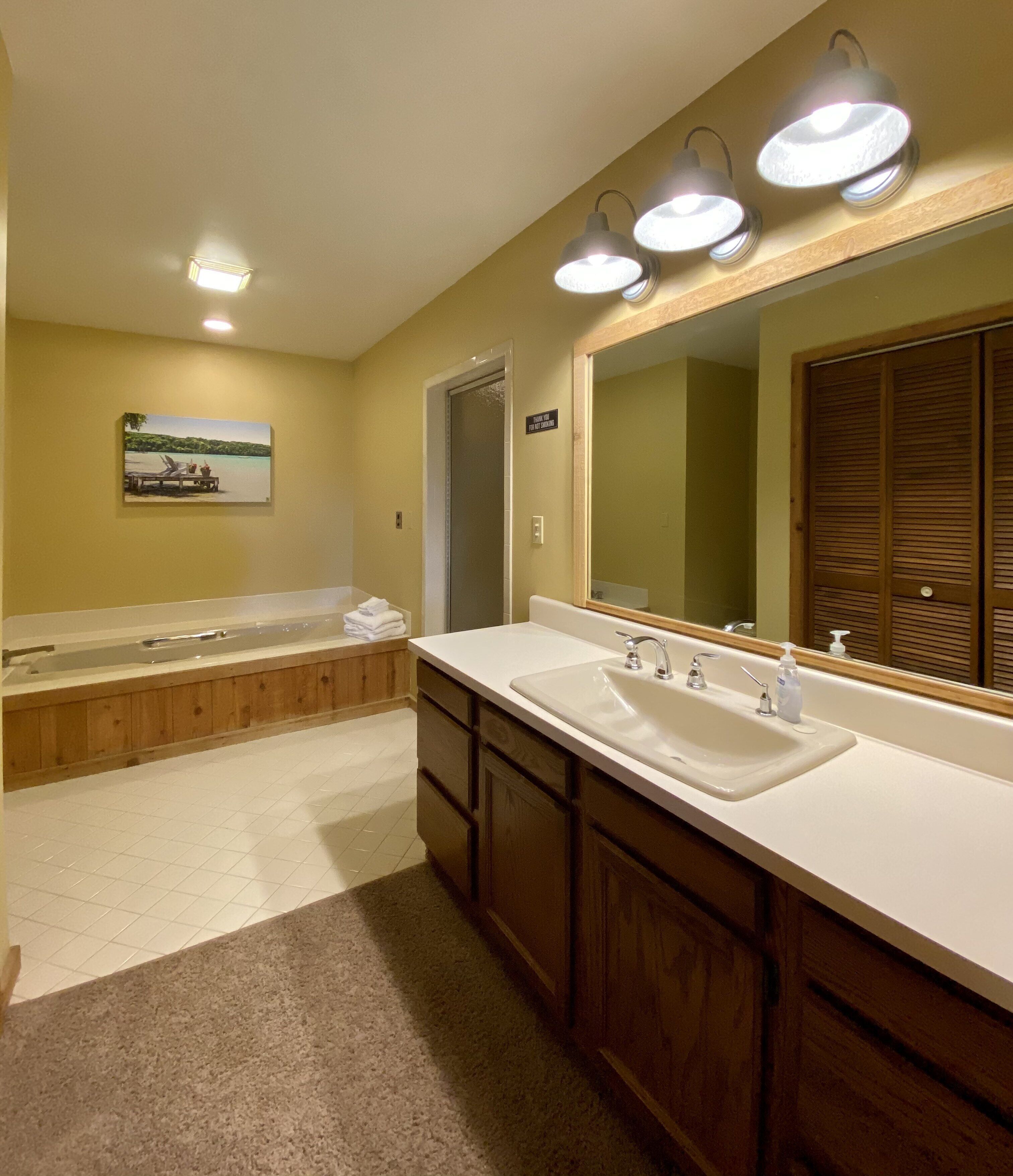 A bathroom with a large bathtub, two sinks, wooden cabinets, a large mirror, and a painting on the wall.