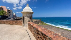 Una fortaleza costera con una estructura en forma de cúpula, un paseo pavimentado y vista al océano.