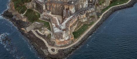 Vista aérea de una fortaleza histórica rodeada por un foso y un paisaje urbano al fondo.