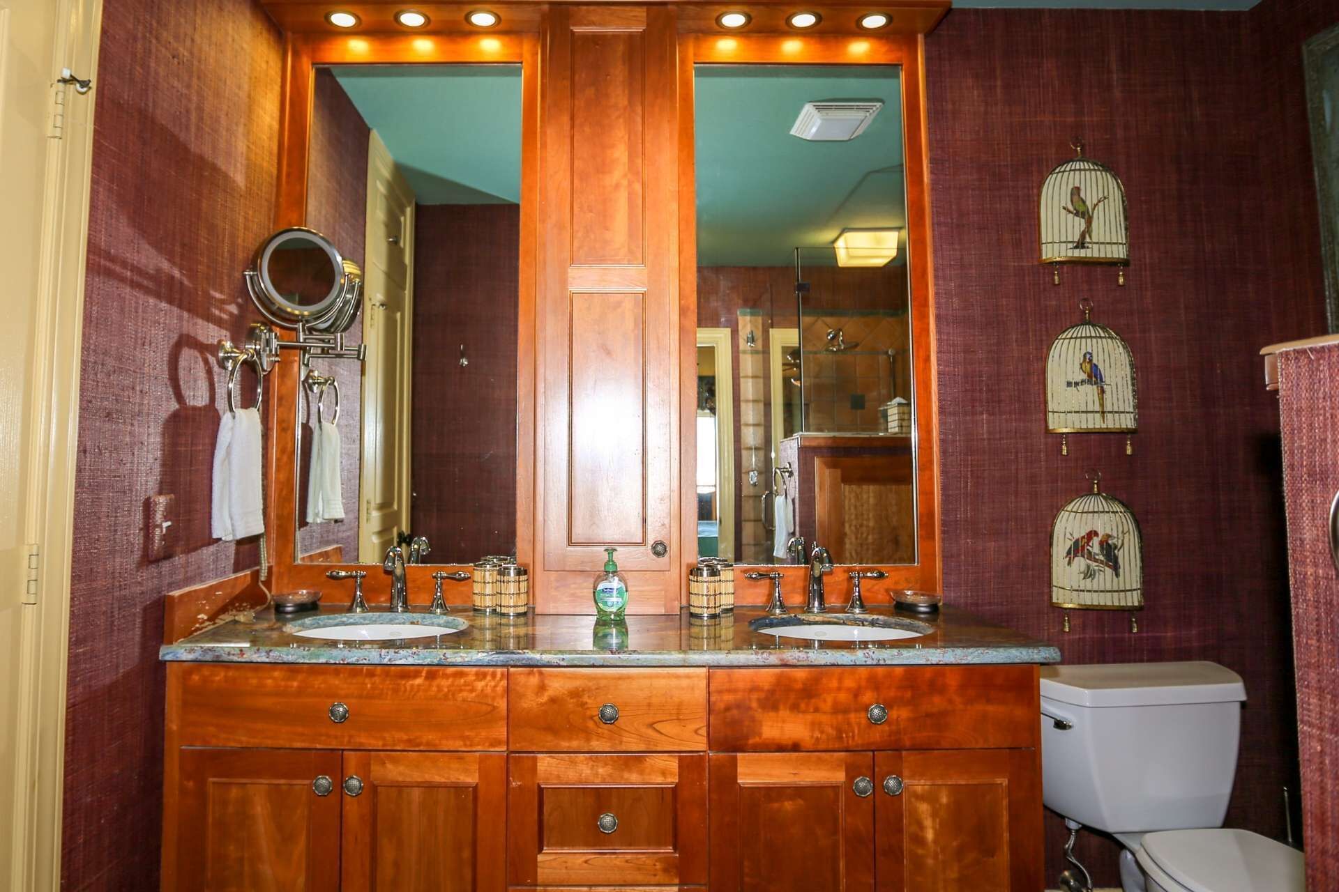 A bathroom with wooden cabinetry, a double sink vanity, a mirror, and birdcage decorations on the wall.