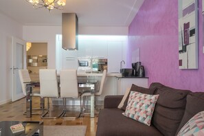 A modern kitchen with white cabinets, a dining area with white chairs, and a brown sofa with patterned cushions.