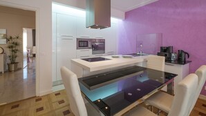 A modern kitchen with white cabinets, a central island, and a purple accent wall. - Violet 2 bedroom apartment (Nice)