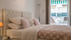 A bedroom with a tufted headboard, a bedside table with a lamp, and a view of the balcony. - Violet 2 bedroom apartment (Nice)