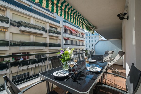 A balcony with a table set for dining, a vase with flowers, and a view of adjacent buildings.