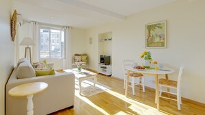 A living room with a sofa, a coffee table, a dining table with chairs, a TV, and a window with curtains. - Yasmin 1 bedroom apartment (Nice)