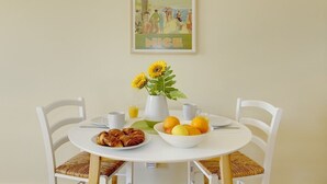 A round dining table with white chairs, a plate of croissants, a bowl of fruit, a vase with sunflowers, and a poster on the wall. - Yasmin 1 bedroom apartment (Nice)