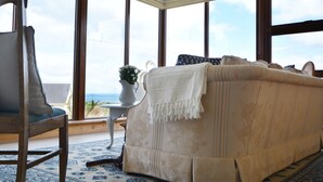 A cozy living room with a large window, a sofa, a chair, and a small table with a vase. - Ard Na Mara 4 bedroom house VRBO (Aughacasla)