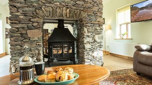 A cozy living room with a stone fireplace, a coffee maker, and a plate of scones on a wooden table. - Ard Na Mara 4 bedroom house VRBO (Aughacasla)