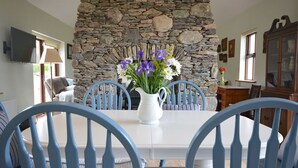 A dining area with a stone fireplace, a white table, and blue chairs. - Ard Na Mara 4 bedroom house VRBO (Aughacasla)