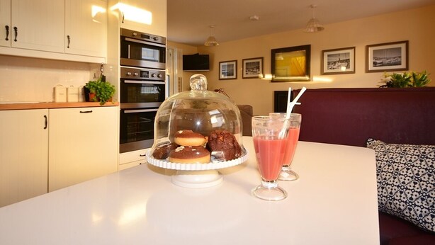 Un coin repas avec une table dressée pour deux personnes, agrémenté d’un présentoir de desserts et de deux verres contenant une boisson rose.