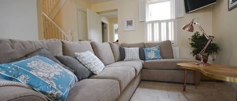 A living room with a sectional sofa, a wooden coffee table, a floor lamp, and a staircase in the background.