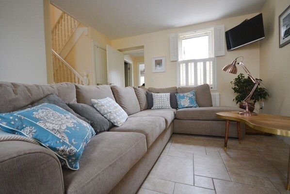 A living room with a sectional sofa, a wooden coffee table, a floor lamp, and a staircase in the background.