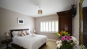 Une chambre à coucher avec un grand lit, une fenêtre avec des stores, une table de chevet avec une lampe et un miroir doté d’un cadre décoratif.